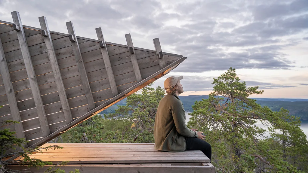 A woman sat on a decking looking out to a view of a lake and greenery (Credit: Martin Edstru00f6m)