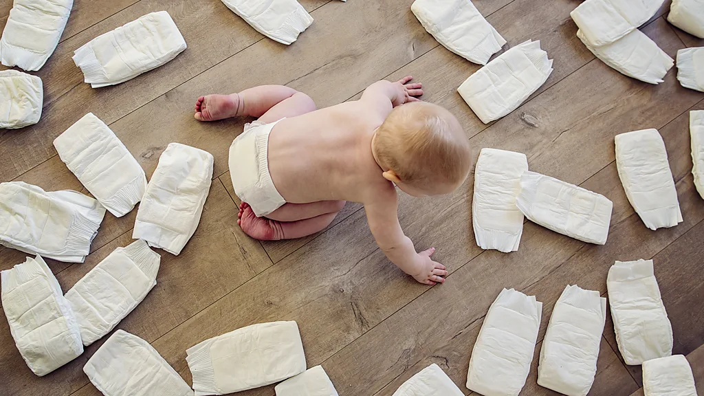 A newborn baby lies curled up in a nappy on a dark-coloured duvet or blanket (Credit: Getty Images)