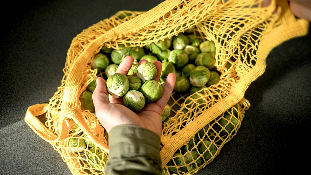 Someone holding a handful of Brussels sprouts, above a yellow mesh bag