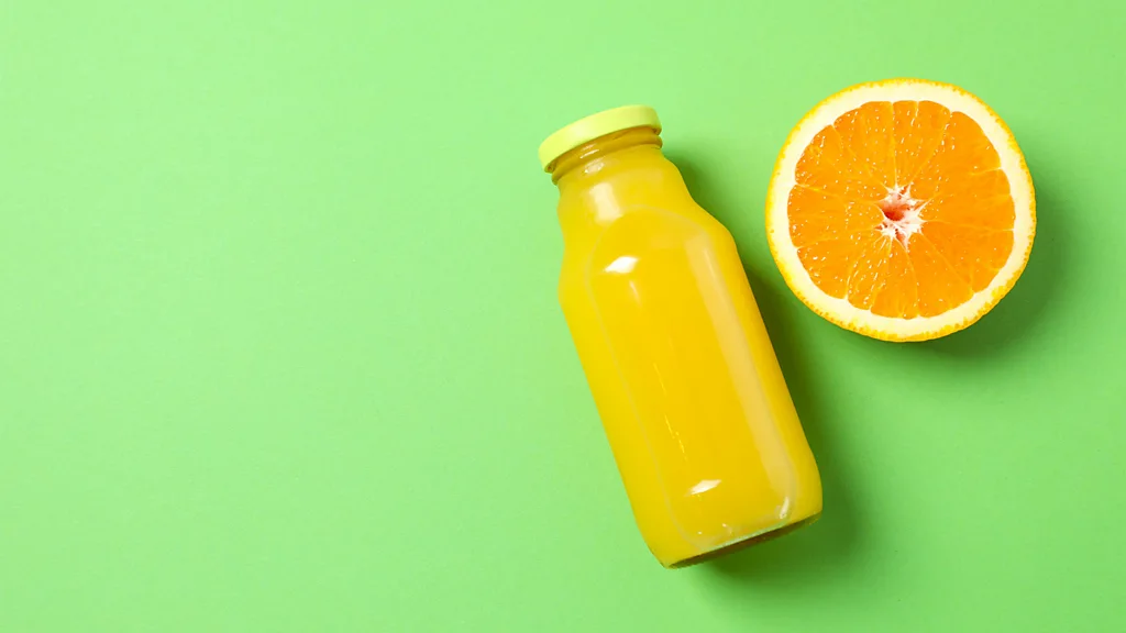 A bottle of orange juice and half an orange on a green background (Credit: Getty Images)