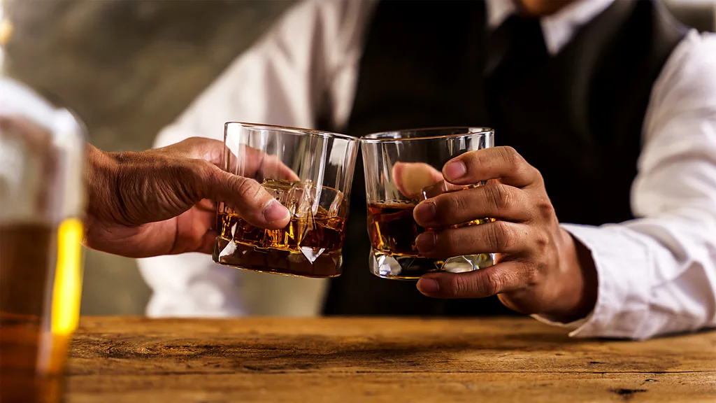 Two men clink glasses of whisky on a table (Credit: Getty Images)