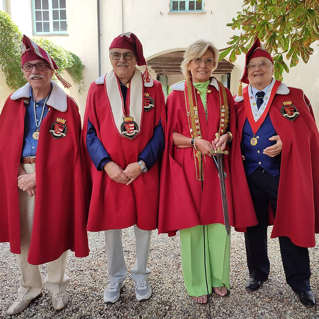 Four members of an Italian culinary confraternity stand side by side outdoors, wearing red ceremonial cloaks and medallions (Credit: Andrea Ivaldi di Gavi)