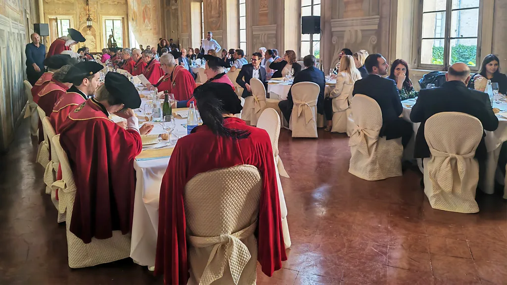 Four members of an Italian culinary confraternity stand side by side outdoors, wearing red ceremonial cloaks and medallions (Credit: Andrea Ivaldi di Gavi)