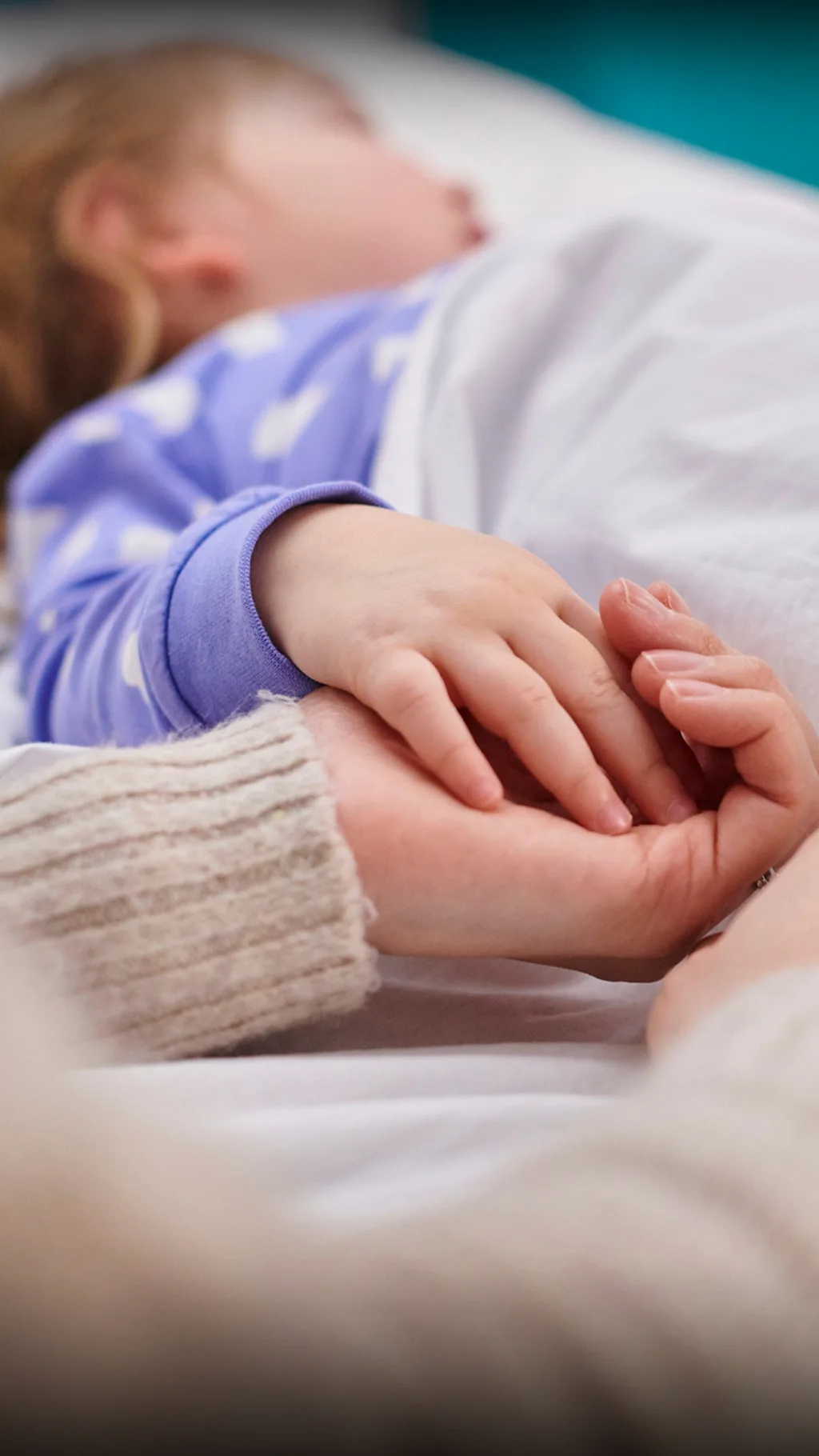 Дитина в ліжку, її за руку тримає рука дорослого