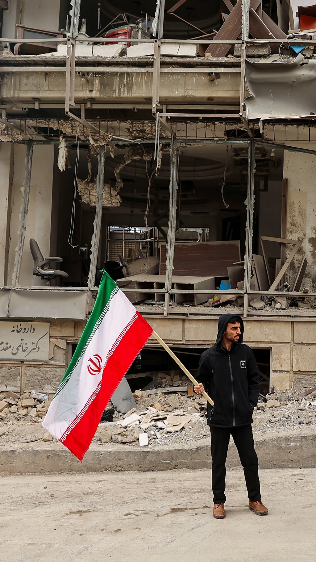 Человек в Тегеране с флагом Ирана у разрушенного здания.