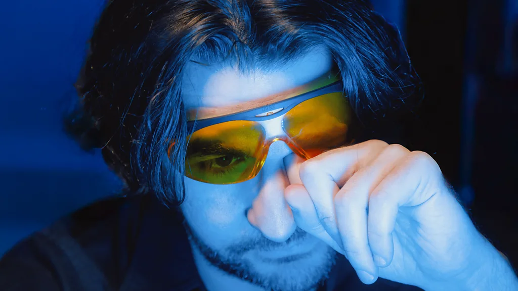 The author Thomas Germain sits holding a smartphone, with blue light shining on him (Credit: Hana Mendel)