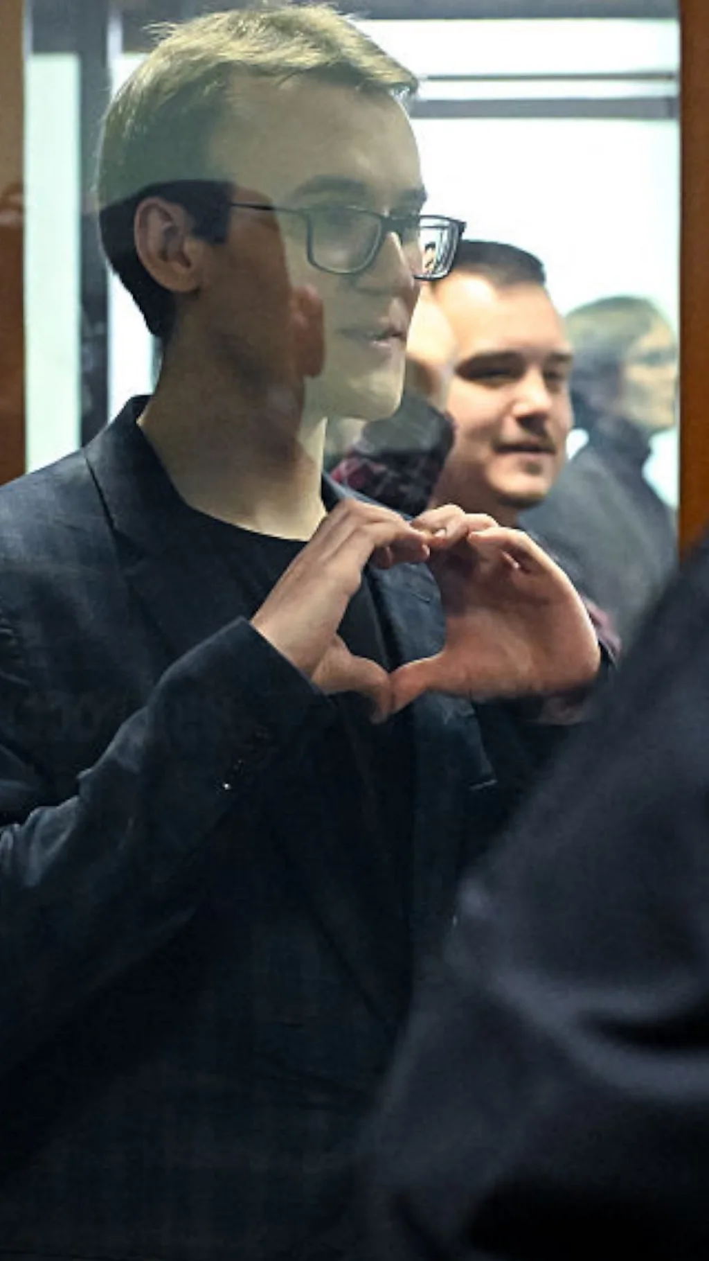 Молодой парень показывает сердечко руками через стекло