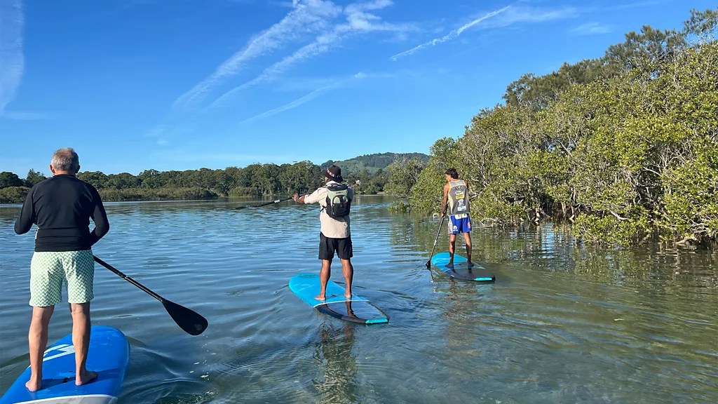Three paddleboarders standing on their boards and paddling 