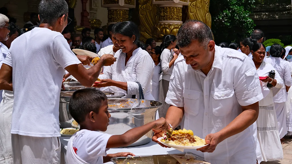 A young boy places food on a plate that a man is holding at a roadside stand in Sri Lanka