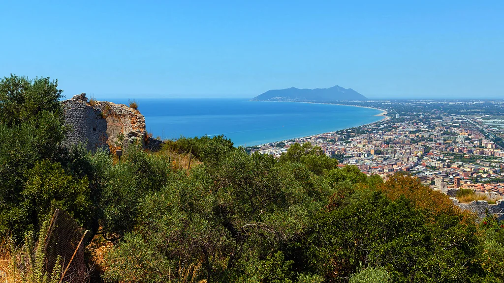 A jagged mountain promontory is at the end of a curving coastline, with Roman ruins in the foreground (Credit: Alamy)