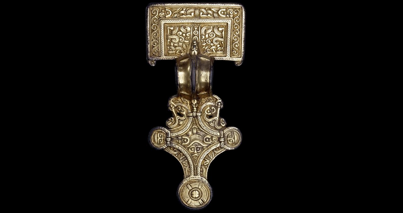A bronze-coloured brooch decorated with multiple faces.