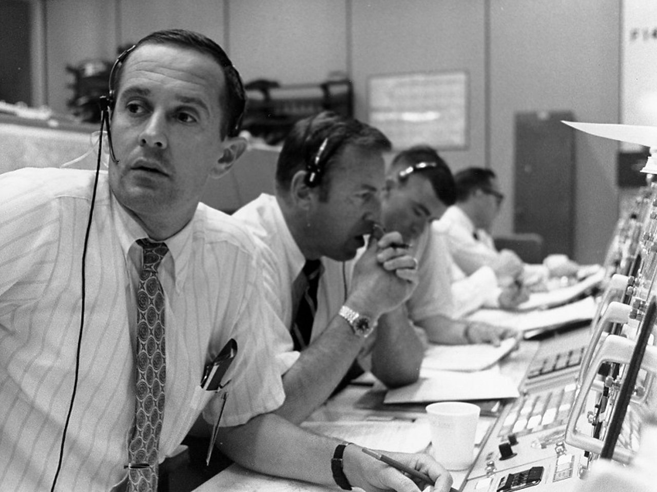 Men at mission control wearing telephone headsets. Left to Right: Charlie Duke; Jim Lovell; Fred Haise.