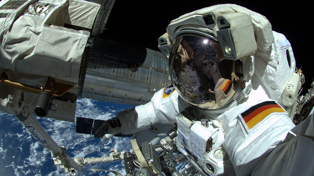 An astronaut outside the ISS with the backdrop of Earth surrounded by space.