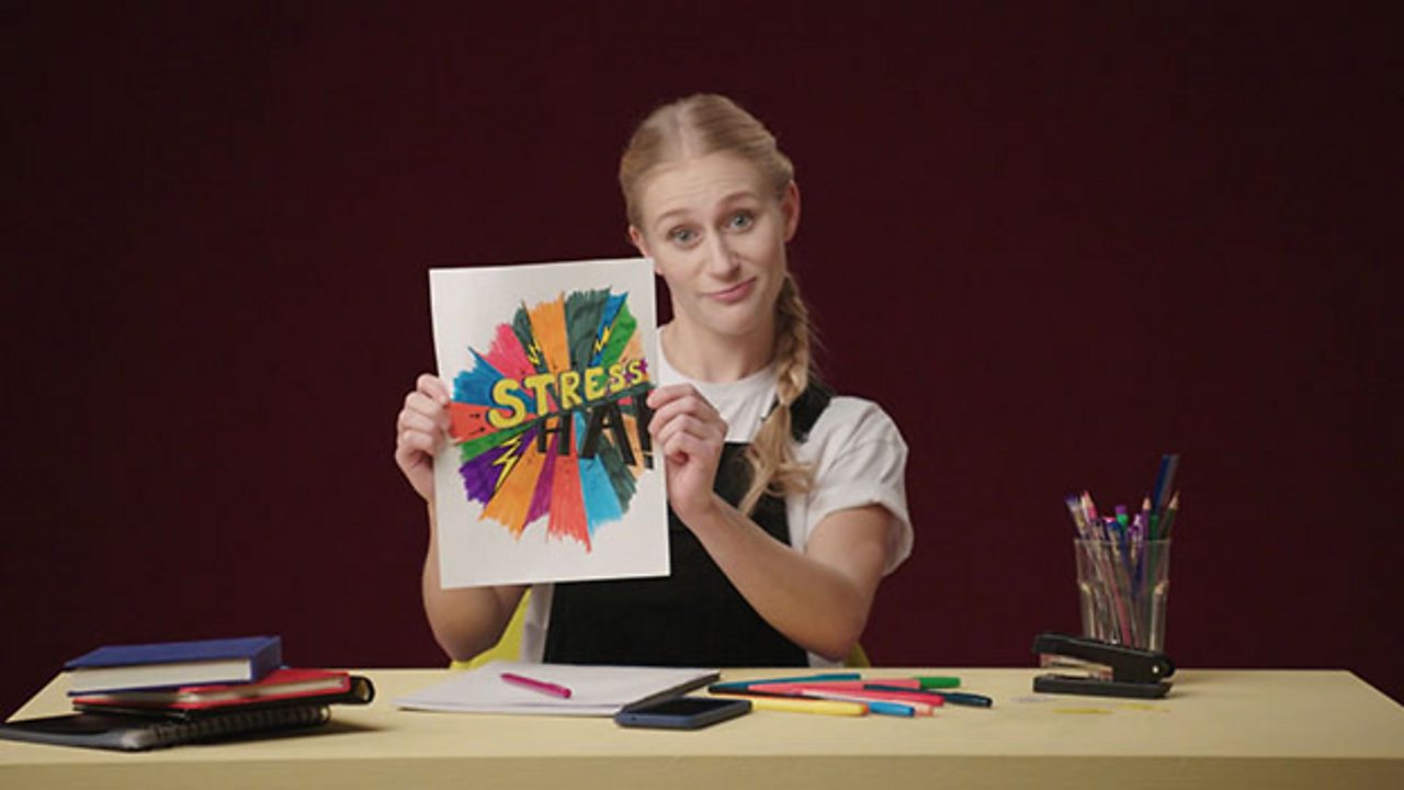 Girl holding up a coloured in image which has the word stress on it