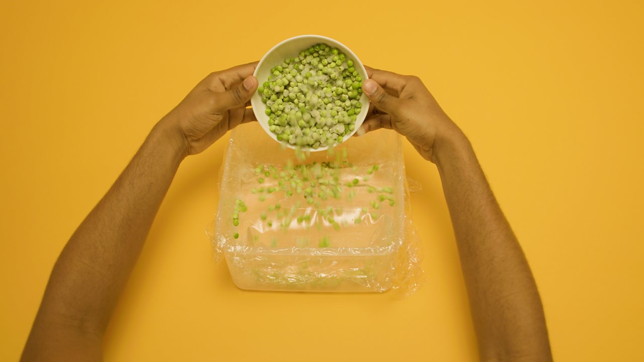 A person tips peas and grapes into the box.