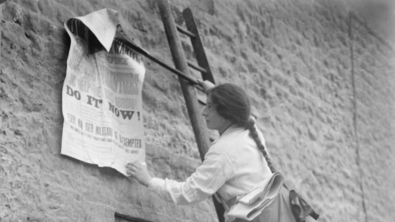Photograph of a girl posting a World War One recruitment poster on the side of a building