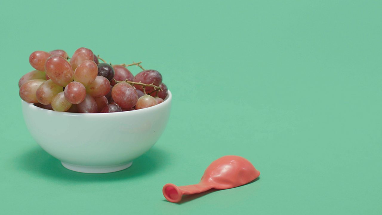 A bowl of grapes on the left and a red balloon (not inflated) on the right.