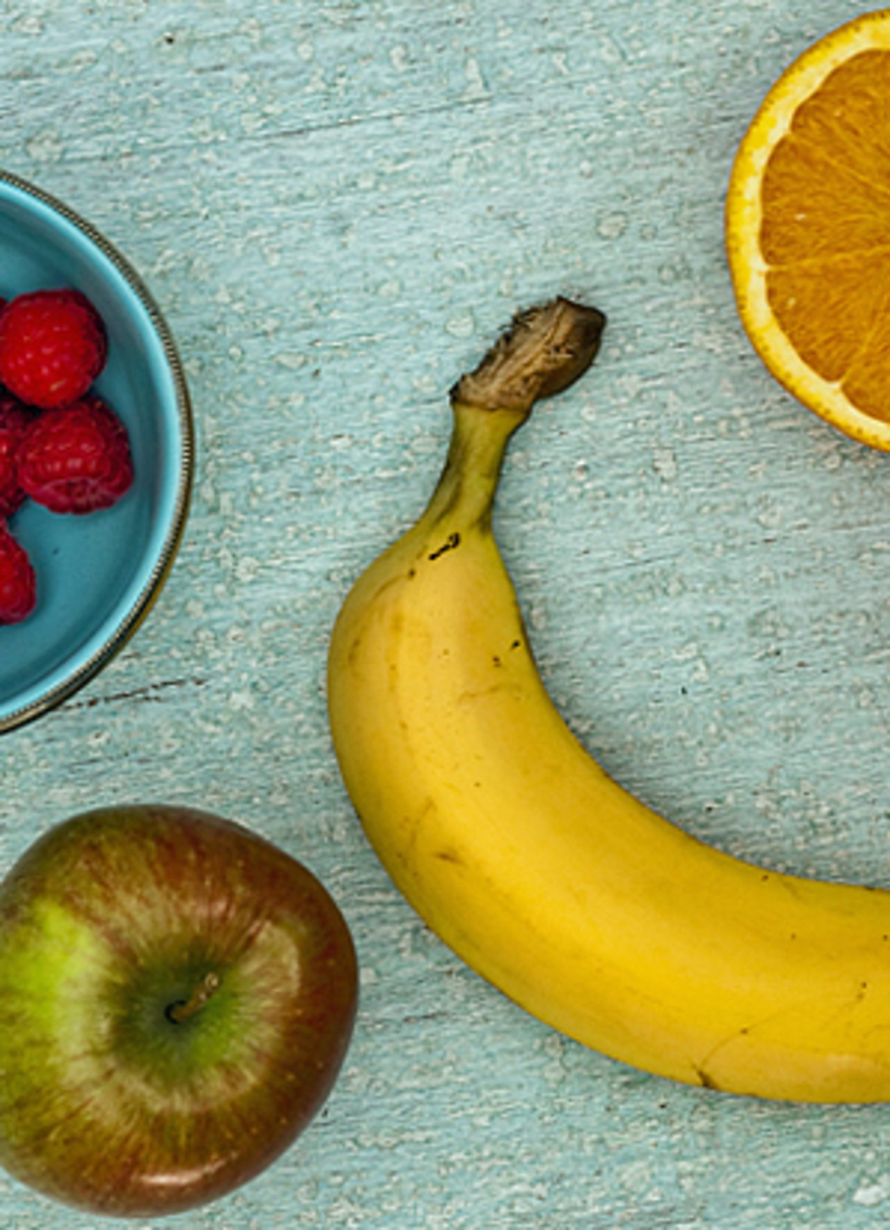 Fruit on table including a banana, apple, orange and raspberries