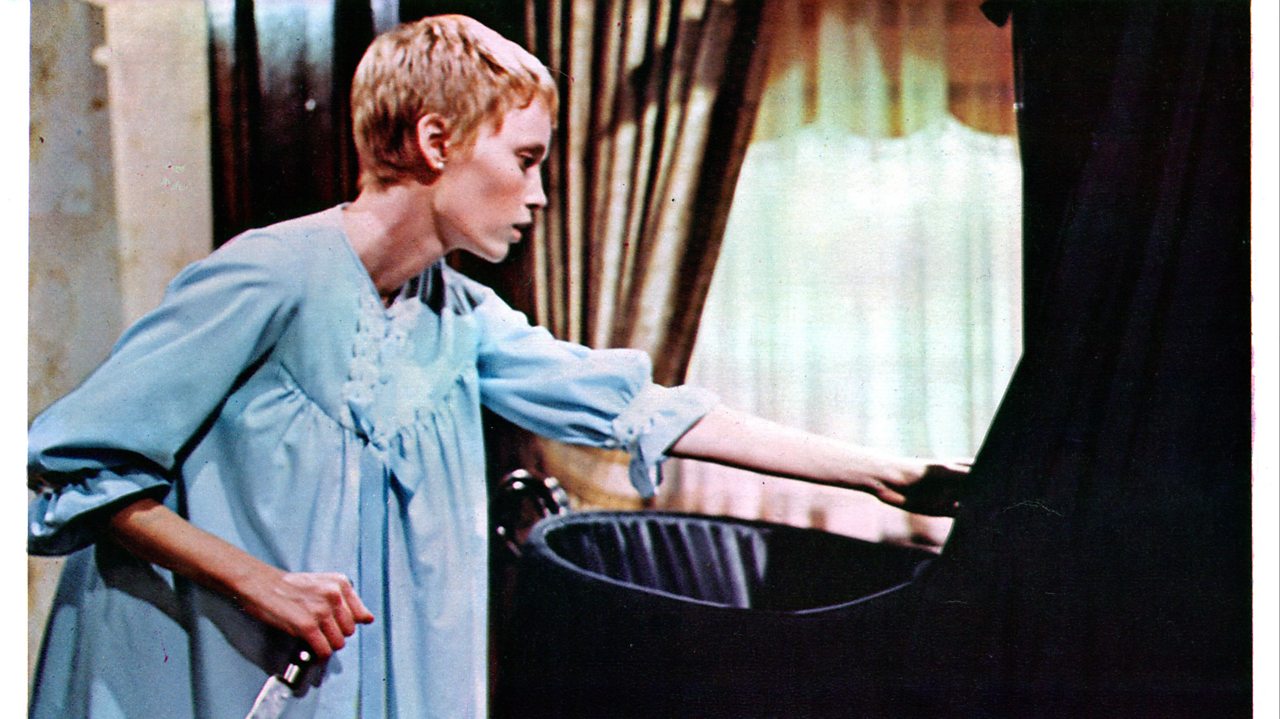 Mia Farrow as Rosemary in 'Rosemary's Baby' leans over a black crib.