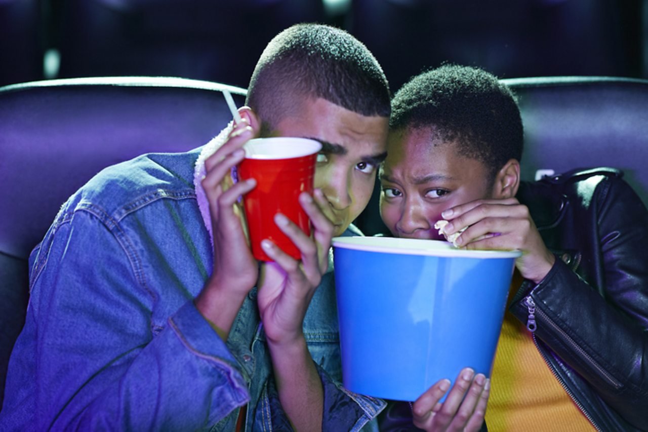 A couple cowers behind their popcorn in a cinema.