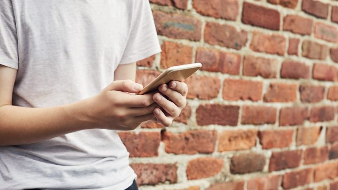 A person (close up) holding a phone next to a brick wall.