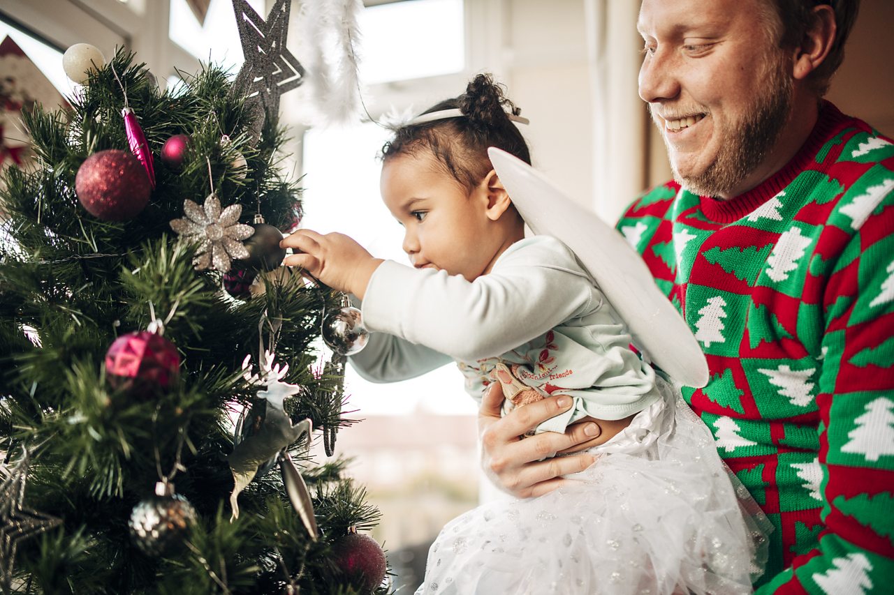 A young girl hangs decorations on a Christmas tree with help from her dad.