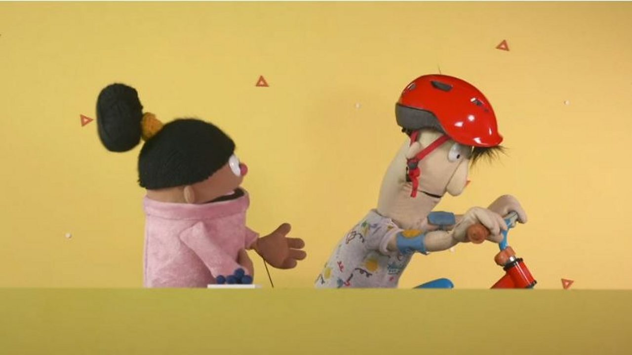 Pip is watching Declan ride his bike. He is wearing a helmet and elbow pads.