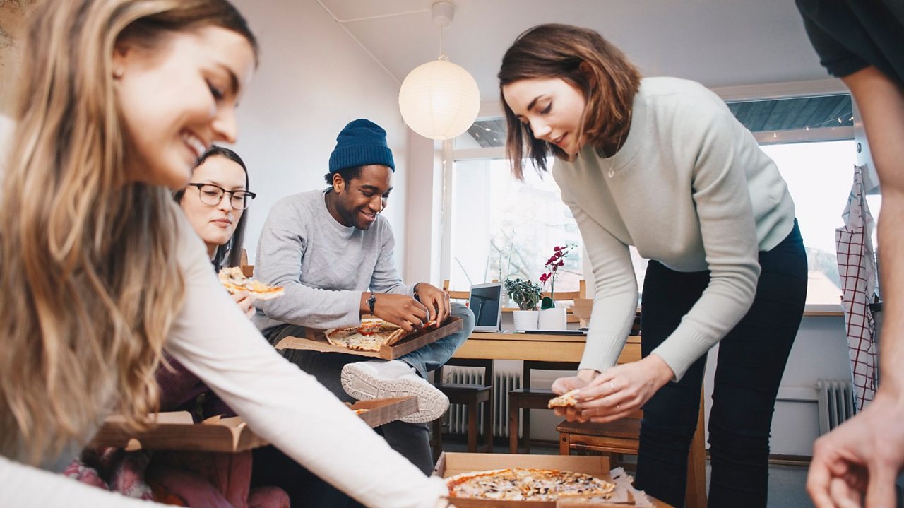Young adults laughing and eating pizza.