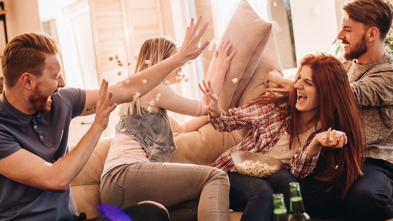 A group of young adults having a pillow fight and throwing popcorn.