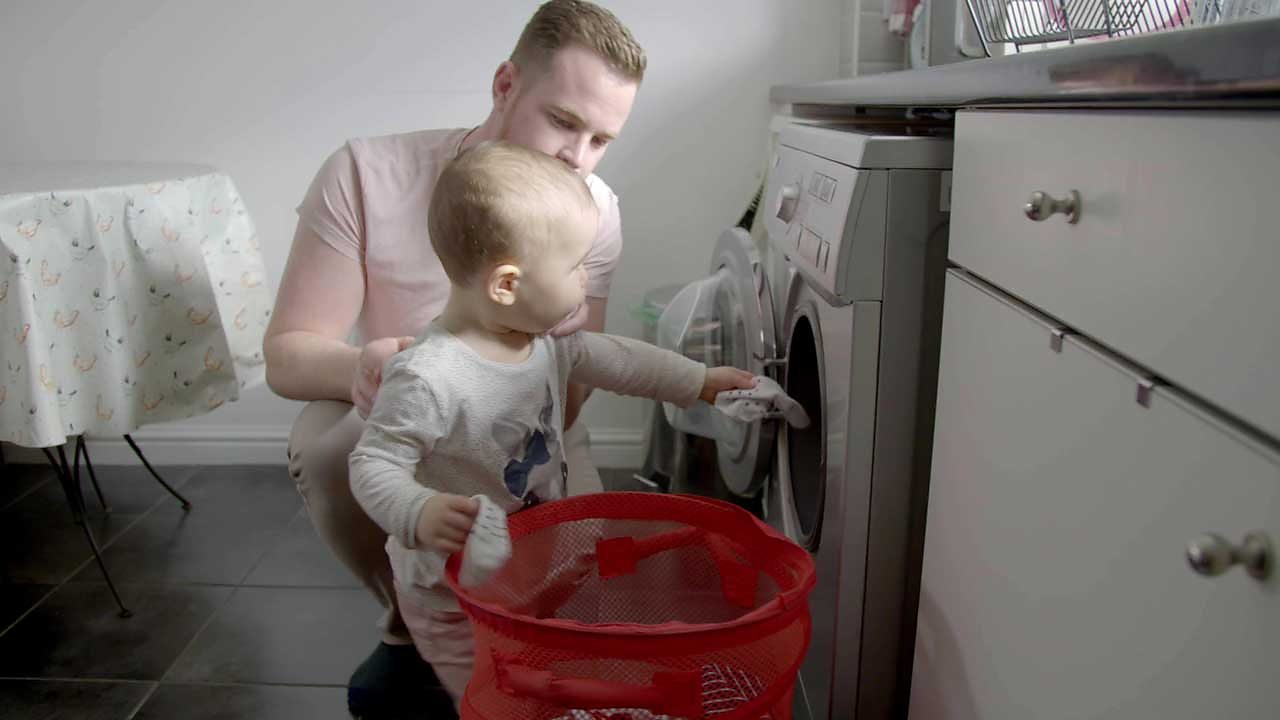 A little girl putting a sock in the washing machine with her dad.