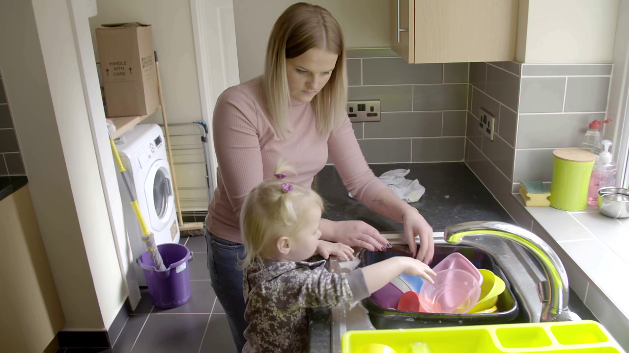 Mum and toddler reaching into a washing up bowl of plastic cups and containers