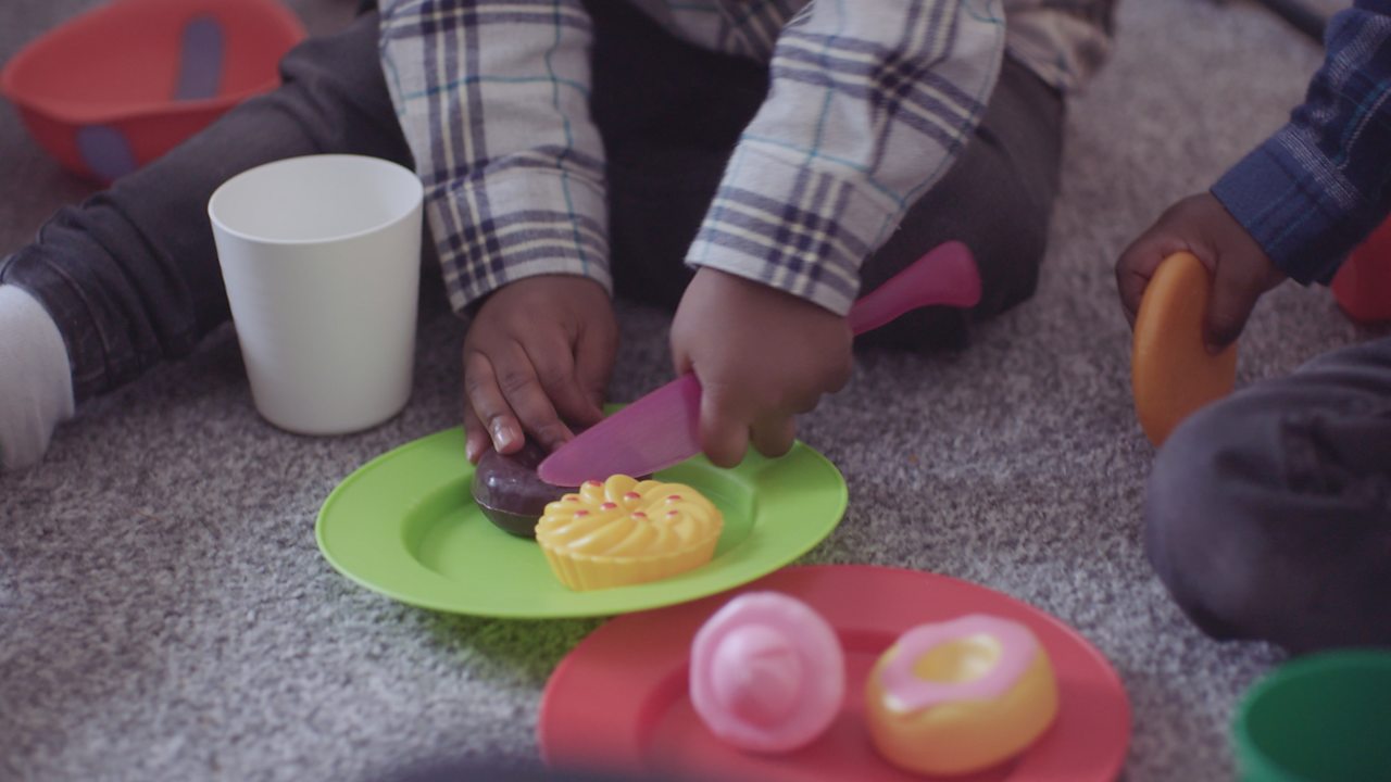 Close up of toddler using plastic cutlery and plates with plastic toy food.