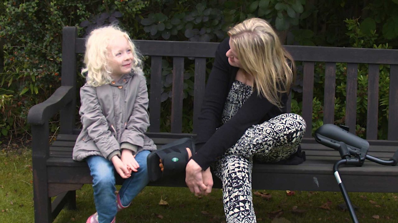 A mum talking to her little girl on a park bench.