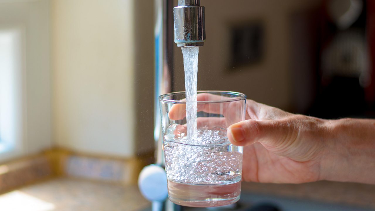 Water is poured from a glass into a tap