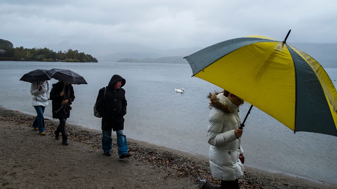 Tourists walking on the shore of Loch Lomond in the rain