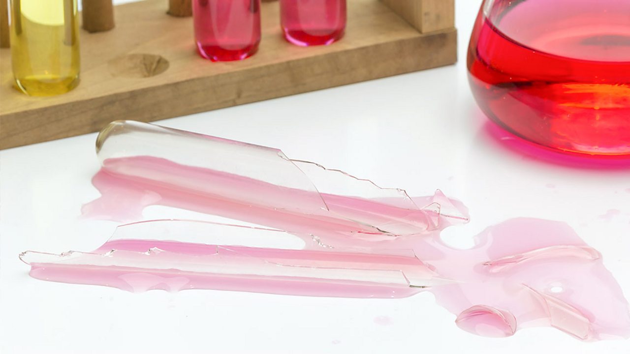 A broken test tube with pink liquid spilling from it and across a white surface.