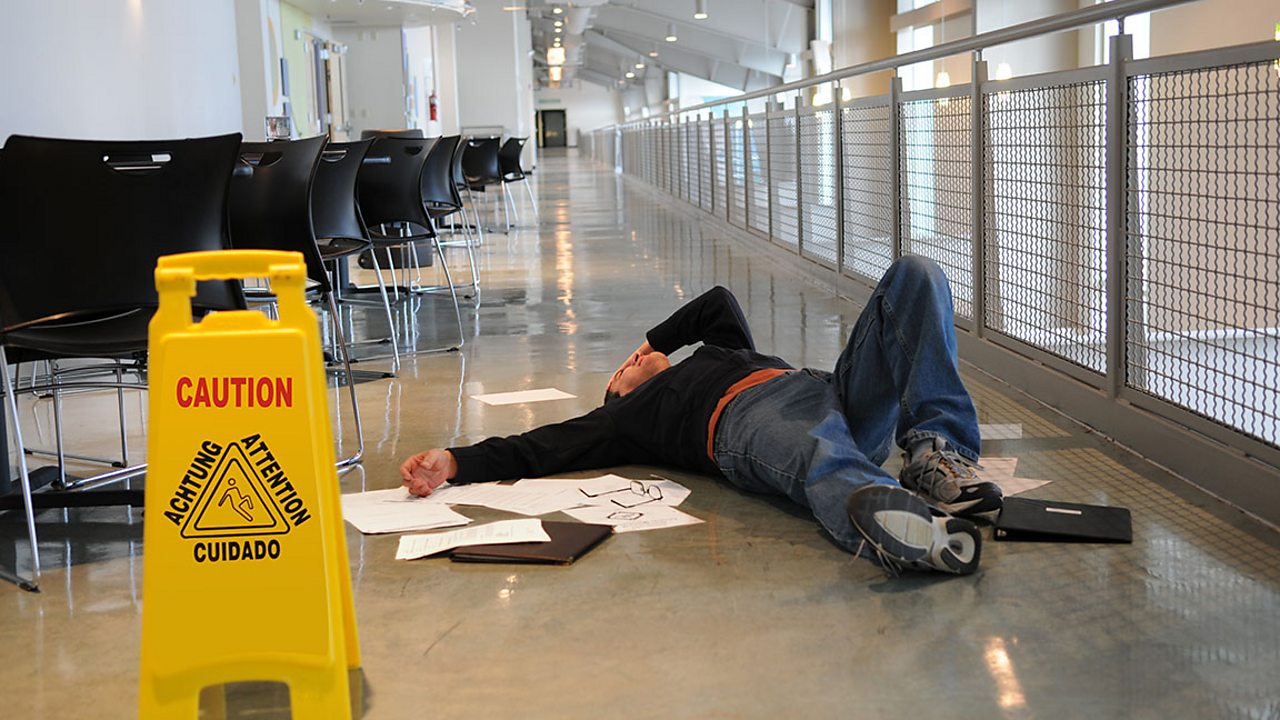 A man lying on wet floor after falling over. There is a sign advising caution as the floor is wet.