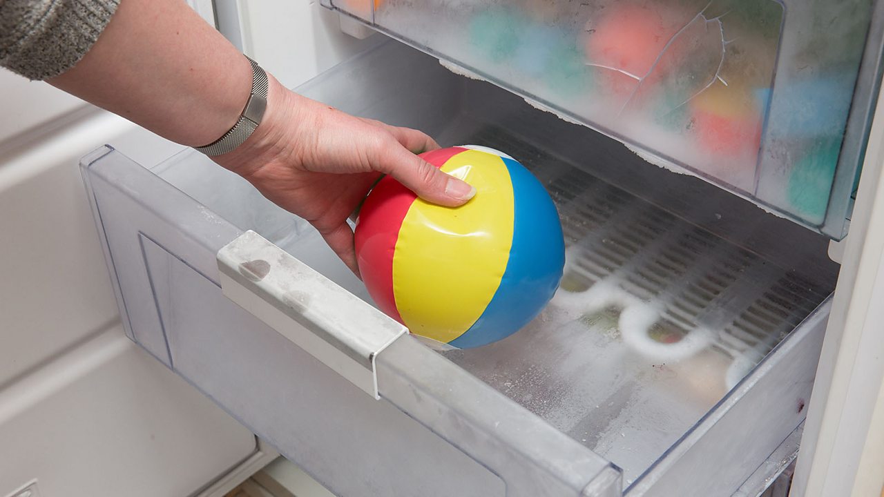 A hand placing a small inflatable ball in the freezer.