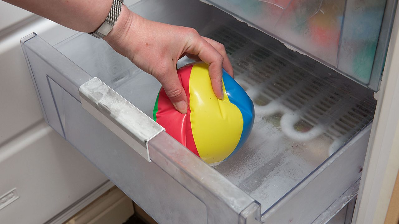 A hand taking a small inflatable ball out of a freezer. The ball is soft