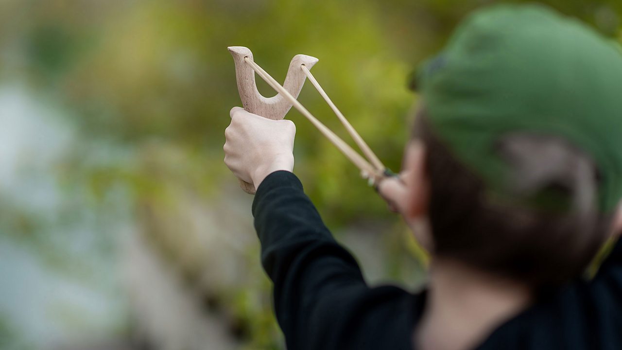 A boy holds a catapult rady to let go. The elastic store in this catapult will be emptied when the boy lets go with his right hand.