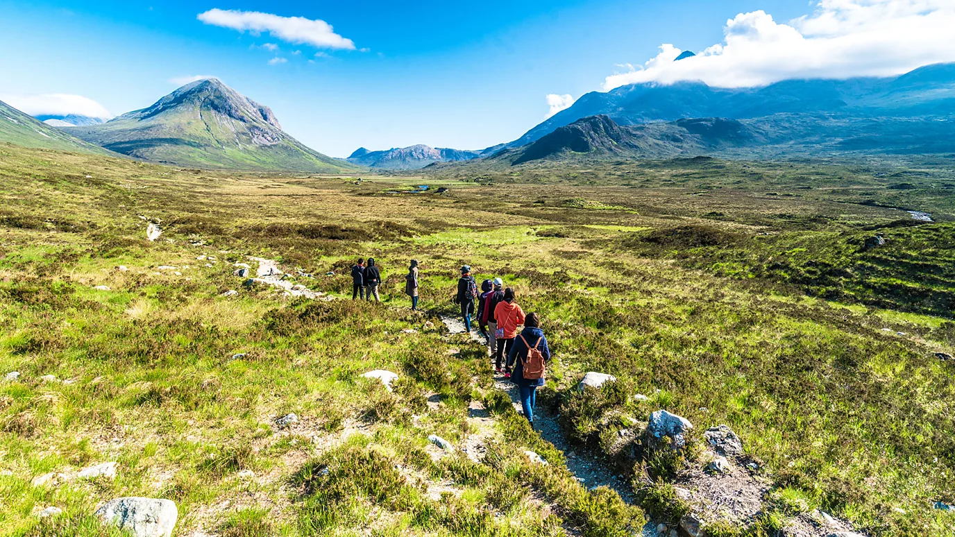 Group of hikers on a trail in a field, mountains in the background. 