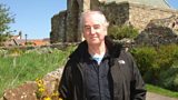 David Almond with St Mary's Church, Lindisfarne in the background
