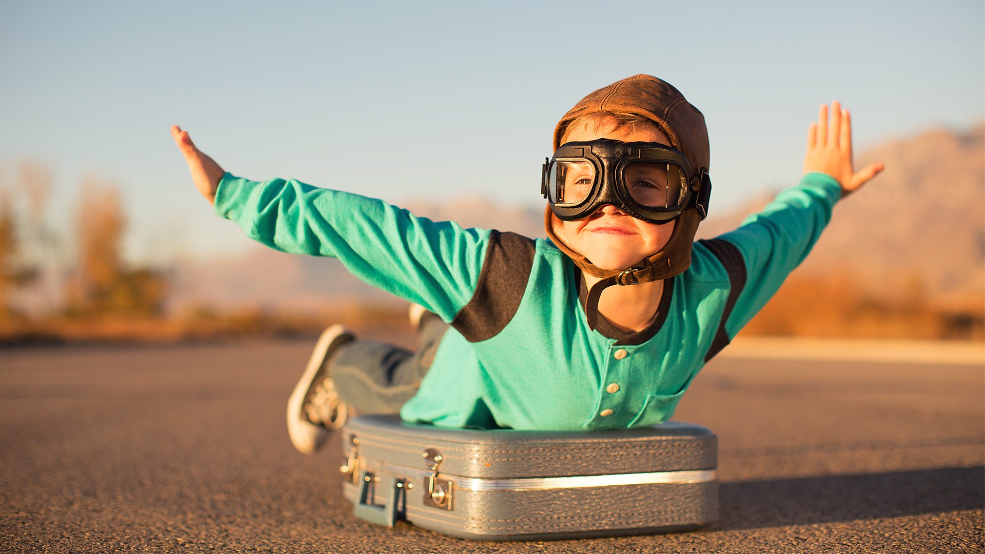 Toddler in pilot goggles lying on a suitcase
