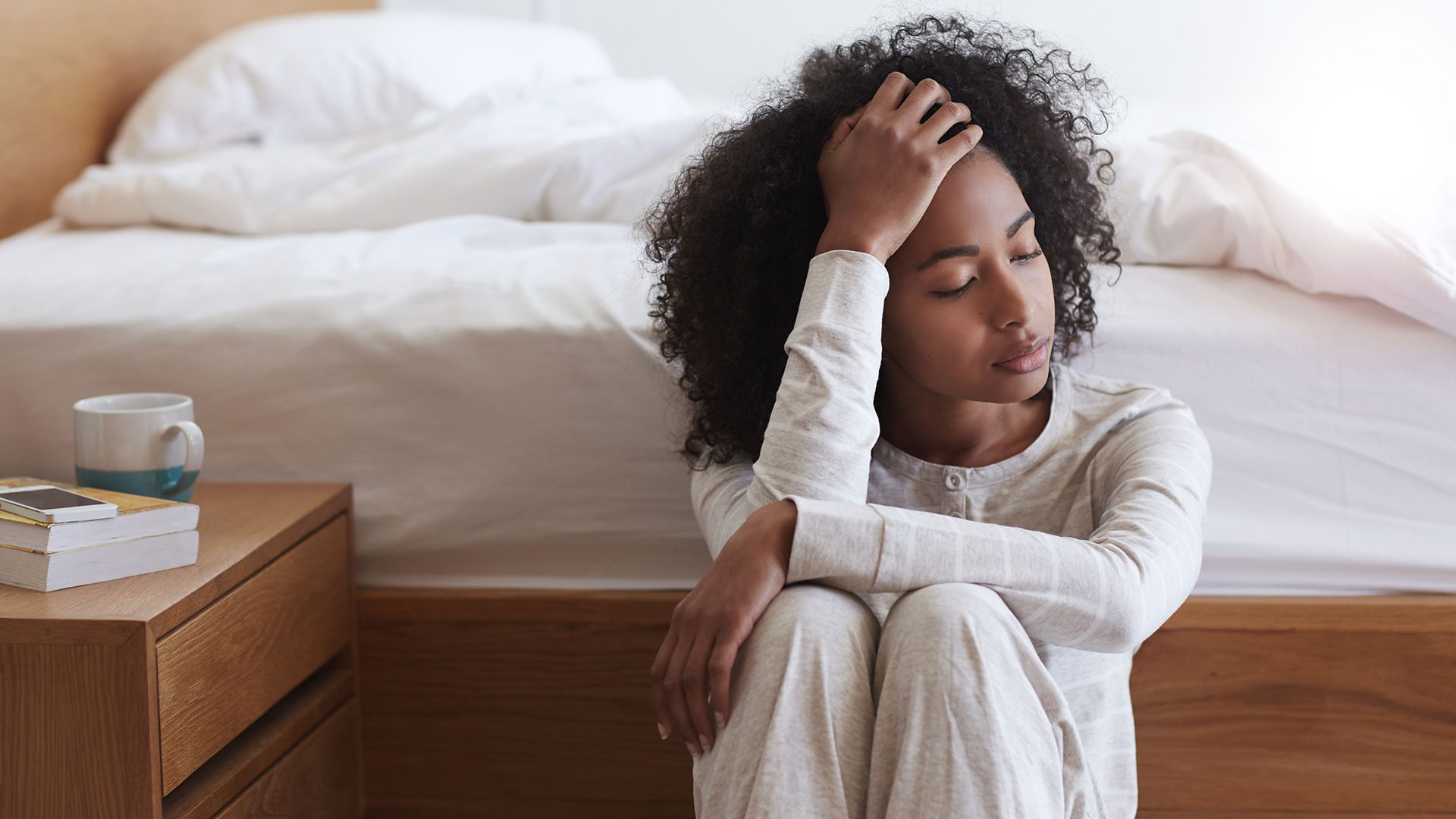 Woman who is sitting next to her bed and hungover