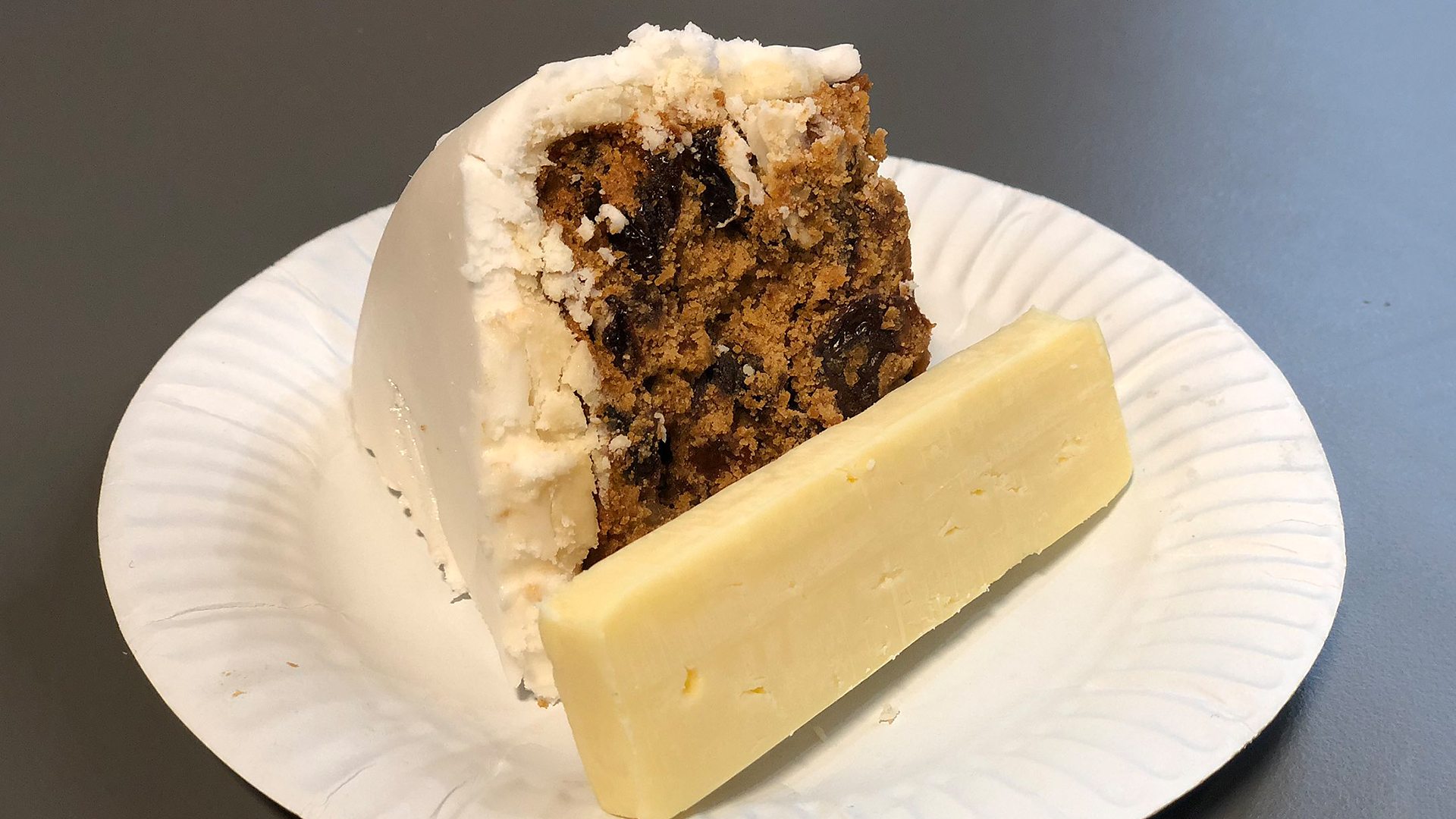 A photo of a slice of Christmas cake and a slice of cheese on a paper plate