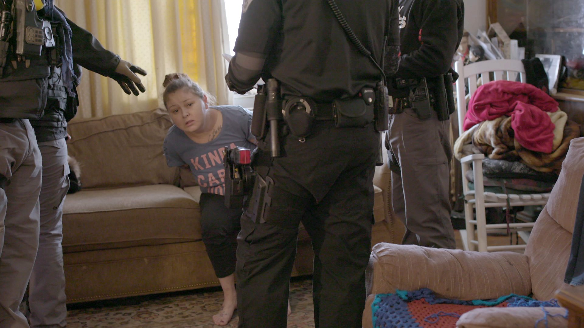 A woman sits on a sofa handcuffed surrounded by three bounty hunters