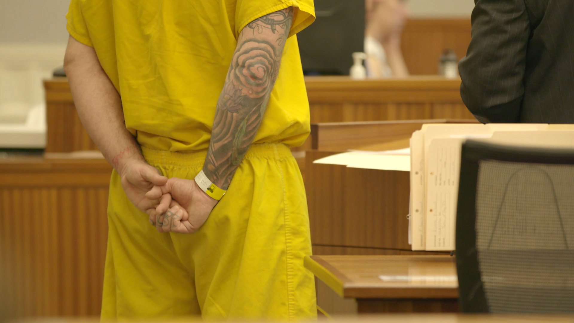 A man stands in court wearing a yellow jumpsuit