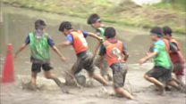 Children play football in a rice paddy