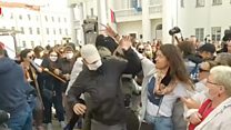 Women try to rip masks off men detaining protesters