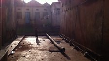 A lone child plays in concrete courtyard of a home in Jinja.